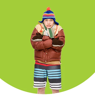 Man wearing a coat, hat and mittens on top and shorts on the bottom