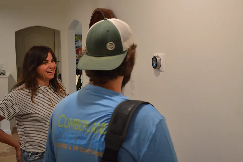 Cumberland Cooling technician looks at thermostat with customer