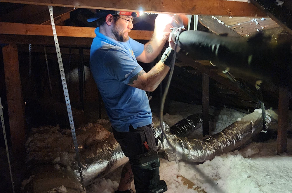 Cumberland Cooling employee working on ductwork in attic