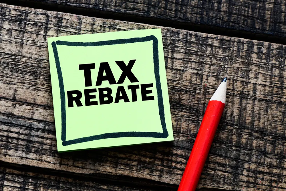 Sticky note with Tax Rebate written on it lying on wood next to pencil